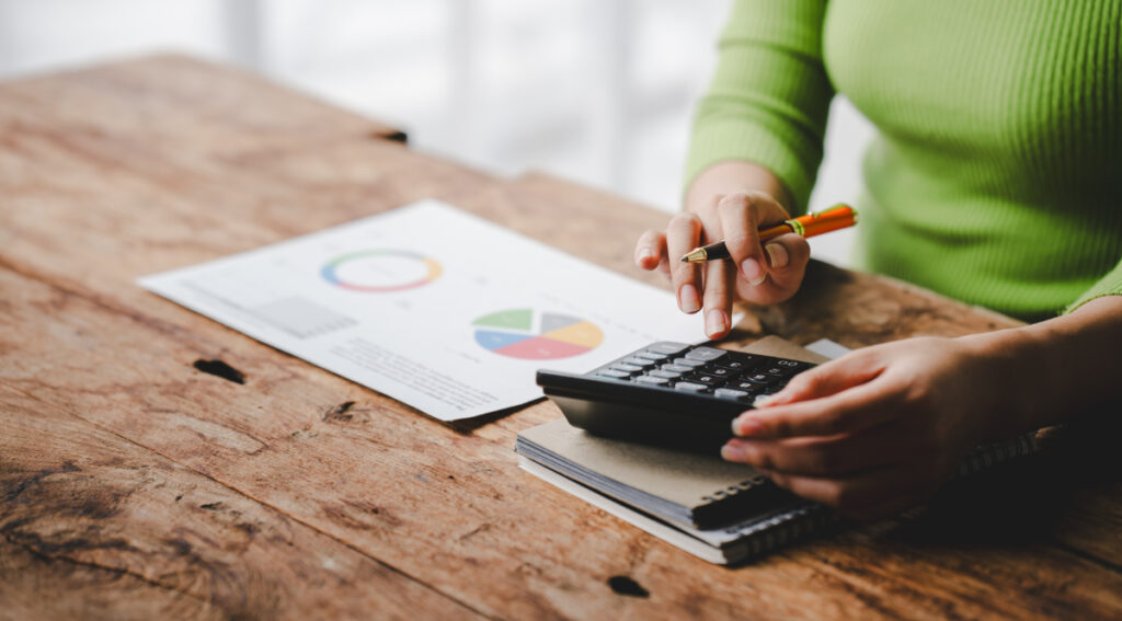 A person using a calculator while reviewing marketing data and budget reports, representing small business marketing strategy.